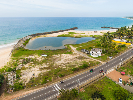 Aerial view of the coastal road and a small lagoon protected by a stone breakwater with palm trees people and vehicles in Peraliya Southern Province Sri Lanka. Aerial view of the coastal road and a small lagoon protected by a stone breakwater with palm trees people and vehicles in Peraliya Southern Province Sri Lanka.