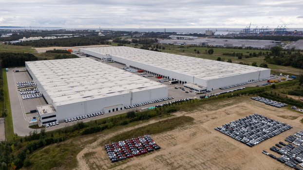 Aerial view of a large logistics warehouse facility with rows of parked cars in the surrounding lots and industrial landscape in Gdansk Poland. Aerial view of a large logistics warehouse facility with rows of parked cars in the surrounding lots and industrial landscape in Gdansk Poland.