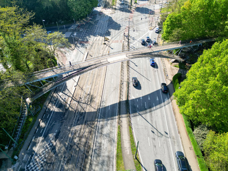 Aerial view of a modern pedestrian bridge spanning over a busy road and tram lines surrounded by lush green trees in Woluwe Saint Pierre Bruxelles Belgium. Aerial view of a modern pedestrian bridge spanning over a busy road and tram lines surrounded by lush green trees in Woluwe Saint Pierre Bruxelles Belgium.