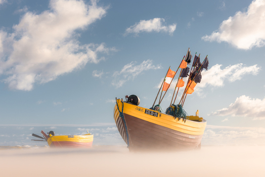View of traditional wooden fishing boats resting on a sandy beach with a misty foreground under a blue cloudy sky in Debki Pomeranian Voivodeship Poland. View of traditional wooden fishing boats resting on a sandy beach with a misty foreground under a blue cloudy sky in Debki Pomeranian Voivodeship Poland.