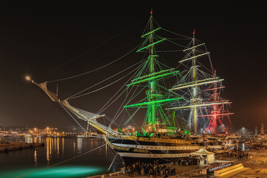 Ancona Marche Italy 12 October 2022 View of the tall ship Amerigo Vespucci illuminated in the colors of the Italian flag docked at the harbor at night with people on the pier.
