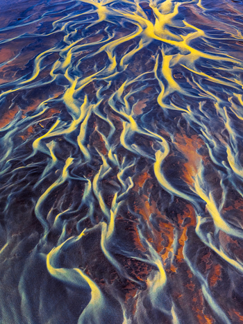 Aerial view of a braided glacial river with vibrant yellow sediment patterns flowing through dark volcanic sand in Iceland. Aerial view of a braided glacial river with vibrant yellow sediment patterns flowing through dark volcanic sand in Iceland.