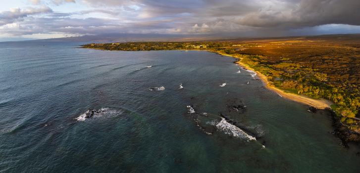 Aerial view of Waikoloa Beach with turquoise waters volcanic coastline and palm trees under a dramatic sunset sky Waikoloa Village Hawaii United States.