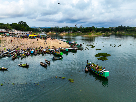 Rangamati Hill District Bangladesh 18 May 2024 Aerial view of Kaptai Lake with wooden boats carrying produce people on the shore and green hills under a cloudy sky.