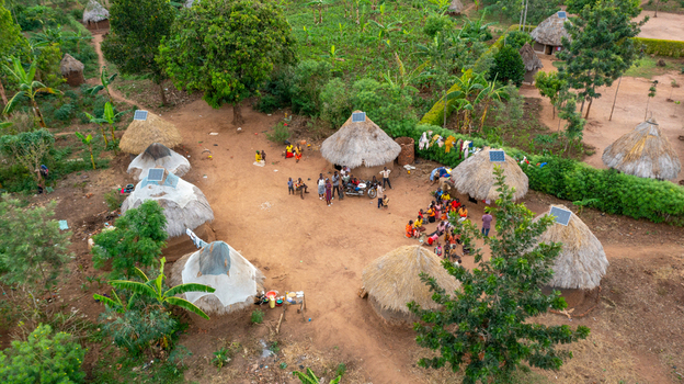 Aerial view of a rural village in Mbale featuring thatched huts with solar panels lush vegetation and local people gathered in the central courtyard in Mbale Eastern Region Uganda. Aerial view of a rural village in Mbale featuring thatched huts with solar panels lush vegetation and local people gathered in the central courtyard in Mbale Eastern Region Uganda.