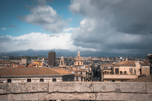 View of sun kissed rooftops and the towering architecture of a city nestled beneath a dramatic sky with distant mountains adding depth Taormina Sicily Italy. View of sun kissed rooftops and the towering architecture of a city nestled beneath a dramatic sky with distant mountains adding depth Taormina Sicily Italy.