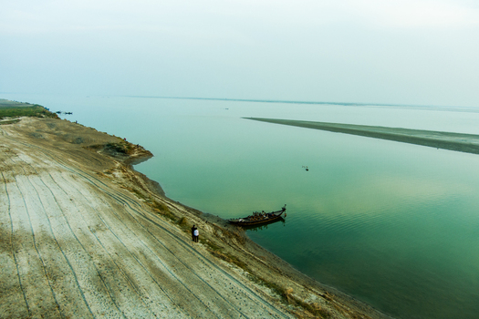 Aerial view of the Padma River bank with a small wooden boat moored near the sandy shore and people standing on the riverbank in Rajshahi Rajshahi Division Bangladesh.