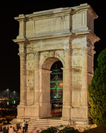 Ancona Marche Italy 12 October 2022 View of the illuminated Arch of Trajan at night with a ship visible through the arch and people in the foreground.