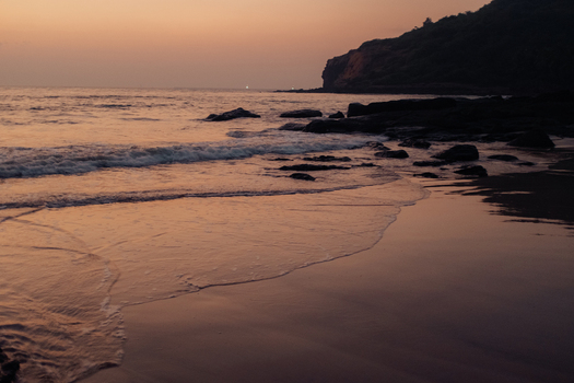 View of the tranquil beach meeting the ocean under a dusky sky with rocks scattered along the shore creating a serene coastal scene Chiplun Maharashtra India. View of the tranquil beach meeting the ocean under a dusky sky with rocks scattered along the shore creating a serene coastal scene Chiplun Maharashtra India.