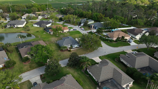 Aerial view of a quiet residential neighborhood with suburban houses manicured green lawns mature trees and a small pond in Plant City Florida United States.