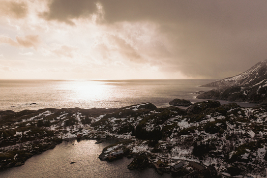 Aerial view of the rugged coastline with snow dusted rocks meeting the vast ocean under a muted sky Reinebringen Nordland Norway.