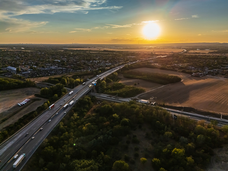 Aerial view of traffic on the M0 ring road near Budapest Hungary with trucks crossing a railway and farmland beside suburban homes in warm evening light. Aerial view of traffic on the M0 ring road near Budapest Hungary with trucks crossing a railway and farmland beside suburban homes in warm evening light.