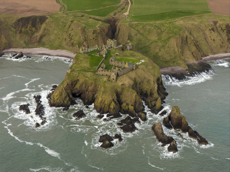 Aerial view of Dunnottar Castle ruins on a dramatic rocky headland with green grass and crashing waves Stonehaven Scotland United Kingdom. Aerial view of Dunnottar Castle ruins on a dramatic rocky headland with green grass and crashing waves Stonehaven Scotland United Kingdom.