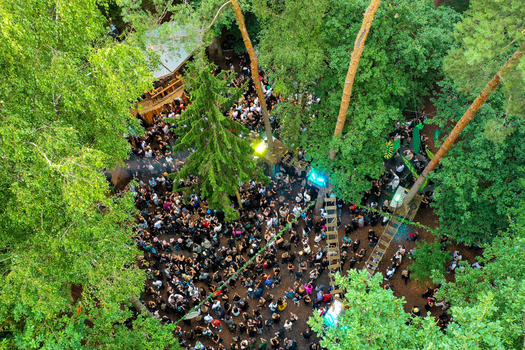 Herzogenaurach Germany 26 July 2025 Aerial view of Open Beatz Festival with a large crowd of people dancing in a forest clearing surrounded by dense green trees.