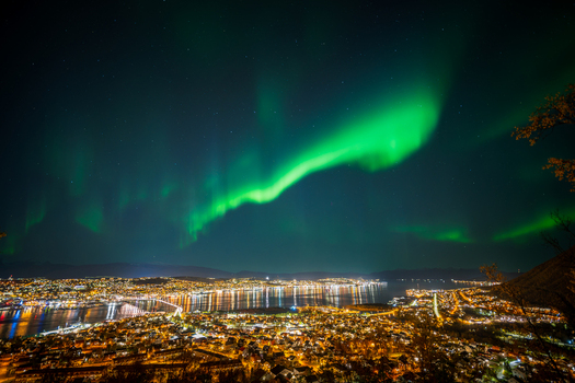 View of the vibrant green aurora borealis illuminating the night sky above the city lights and harbor of Tromso Troms Norway. View of the vibrant green aurora borealis illuminating the night sky above the city lights and harbor of Tromso Troms Norway.