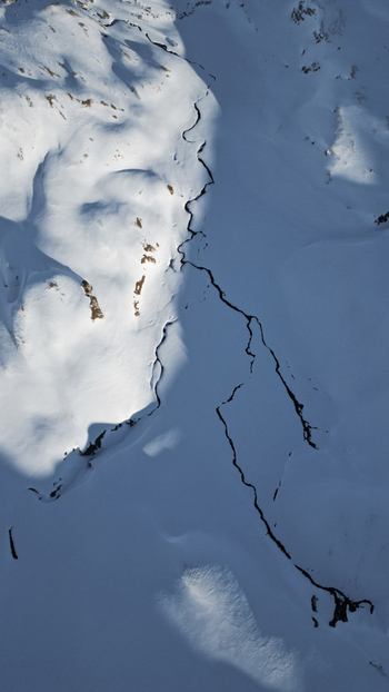 Aerial view of a stark snow dusted landscape carved by a meandering stream casting long shadows across the frozen terrain Anniviers Switzerland. Aerial view of a stark snow dusted landscape carved by a meandering stream casting long shadows across the frozen terrain Anniviers Switzerland.