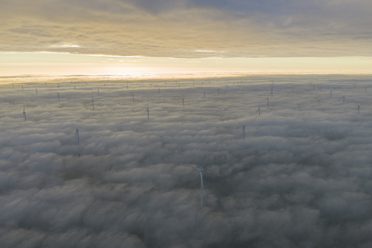 Aerial view of wind turbines poking through a dense blanket of clouds under a golden sunrise sky in Netherlands. Aerial view of wind turbines poking through a dense blanket of clouds under a golden sunrise sky in Netherlands.