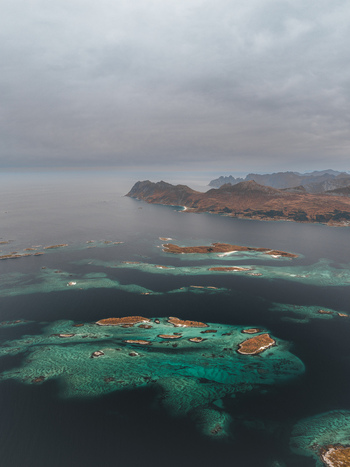 Aerial view of the rugged coastline and turquoise waters surrounding the island of Senja with rocky islets under a cloudy sky in Senja Troms Norway.