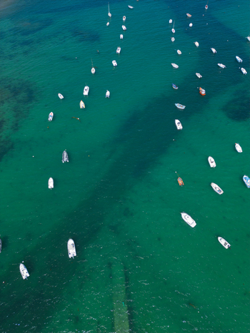 Aerial view of numerous small white boats anchored in the clear turquoise waters near Plage de Port Blanc in Penvenan Bretagne France. Aerial view of numerous small white boats anchored in the clear turquoise waters near Plage de Port Blanc in Penvenan Bretagne France.