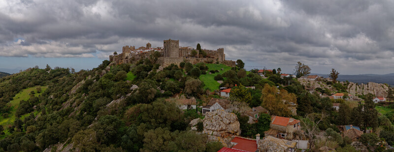 Aerial view of a medieval castle perched atop a hill amidst the lush green foliage under a dramatic cloudy sky Castellar de la Frontera Andalusia Spain. Aerial view of a medieval castle perched atop a hill amidst the lush green foliage under a dramatic cloudy sky Castellar de la Frontera Andalusia Spain.