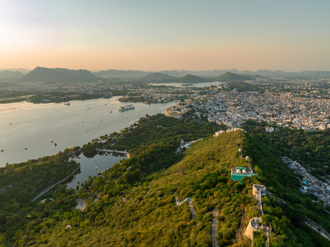 Aerial view of Udaipur the City of Lakes featuring Lake Pichola surrounding hills lush greenery and the dense urban landscape under a soft sunset sky in Udaipur Rajasthan India.