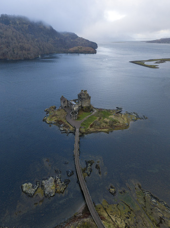 Aerial view of Eilean Donan Castle on its tidal island with the stone bridge and misty highlands in the background Dornie Scotland United Kingdom.