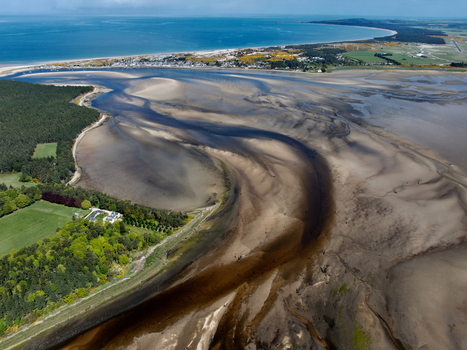 Aerial view of Findhorn Bay showing the winding sandy estuary at low tide with the coastal village and blue sea in the distance Findhorn Scotland United Kingdom. Aerial view of Findhorn Bay showing the winding sandy estuary at low tide with the coastal village and blue sea in the distance Findhorn Scotland United Kingdom.