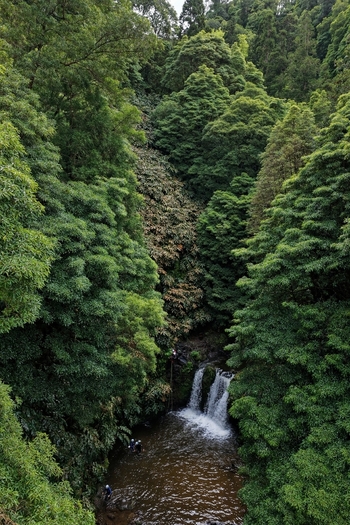 Aerial view of Parque Natural da Ribeira dos Caldeiroes waterfall surrounded by lush green forest with people at the base in Achada Acores Portugal. Aerial view of Parque Natural da Ribeira dos Caldeiroes waterfall surrounded by lush green forest with people at the base in Achada Acores Portugal.