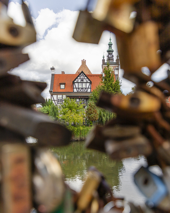 View of a historic half timbered building with a red roof and tower framed by love locks on a bridge over a canal in Gdansk Pomeranian Voivodeship Poland. View of a historic half timbered building with a red roof and tower framed by love locks on a bridge over a canal in Gdansk Pomeranian Voivodeship Poland.
