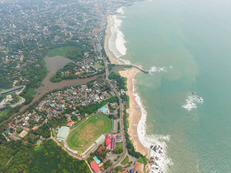 Aerial view of the coastline featuring a green sports stadium sandy beaches and dense urban housing surrounded by lush tropical vegetation in Galle Southern Province Sri Lanka. Aerial view of the coastline featuring a green sports stadium sandy beaches and dense urban housing surrounded by lush tropical vegetation in Galle Southern Province Sri Lanka.