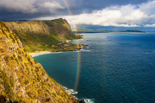 View of Makapuu Point Lighthouse Trail with a vibrant rainbow over the rugged coastline steep cliffs and deep blue ocean in Waimanalo Hawaii United States. View of Makapuu Point Lighthouse Trail with a vibrant rainbow over the rugged coastline steep cliffs and deep blue ocean in Waimanalo Hawaii United States.