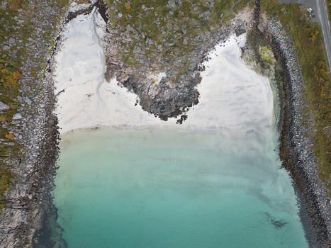 Aerial view of Rorvikstranda beach with its white sand and turquoise water nestled between rugged rocky cliffs in Henningsvaer Nordland Norway.