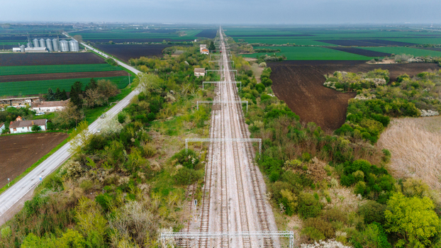 Aerial view of a long railway track cutting through green fields and trees with a cluster of silos visible in the distance Sremska Mitrovica Vojvodina Serbia. Aerial view of a long railway track cutting through green fields and trees with a cluster of silos visible in the distance Sremska Mitrovica Vojvodina Serbia.