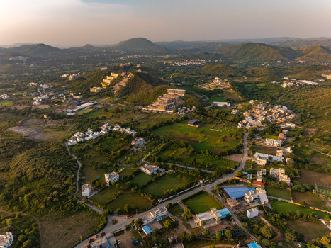 Aerial view of the landscape in Udaipur featuring rolling hills green fields and scattered residential buildings during the golden hour in Udaipur Rajasthan India.