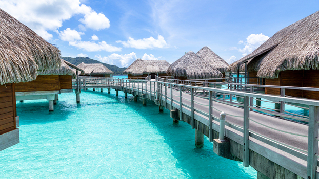 View of overwater bungalows with thatched roofs connected by a wooden walkway over the turquoise lagoon in Bora Bora Leeward Islands French Polynesia.