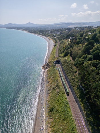 Aerial view of the Dalkey coastal railway line with a train emerging from a tunnel running along the rocky coastline and the Irish Sea in Dublin County Dublin Ireland. Aerial view of the Dalkey coastal railway line with a train emerging from a tunnel running along the rocky coastline and the Irish Sea in Dublin County Dublin Ireland.