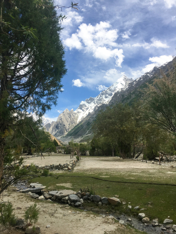 View of the Hushe River Valley with snow capped mountains lush green trees a small stream and a blue sky in Saling Gilgit Pakistan. View of the Hushe River Valley with snow capped mountains lush green trees a small stream and a blue sky in Saling Gilgit Pakistan.