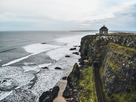 Aerial view of Mussenden Temple perched on a cliff edge overlooking the Atlantic Ocean with a railway line running below in Coleraine Northern Ireland United Kingdom. Aerial view of Mussenden Temple perched on a cliff edge overlooking the Atlantic Ocean with a railway line running below in Coleraine Northern Ireland United Kingdom.