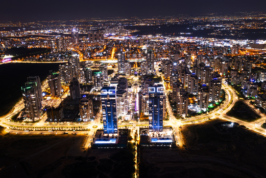 Aerial view of the illuminated skyline at night featuring modern high rise residential towers glowing street lights and urban infrastructure in Netanya Center District Israel. Aerial view of the illuminated skyline at night featuring modern high rise residential towers glowing street lights and urban infrastructure in Netanya Center District Israel.