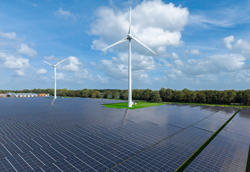 Aerial view of a large solar farm with wind turbines in a rural landscape under a blue sky with clouds in Warmenhuizen North Holland Netherlands.