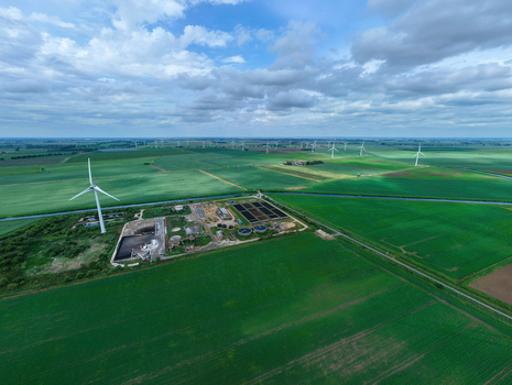 Aerial view of the March Anglian Water sewage treatment plant surrounded by green fields and wind turbines under a cloudy sky in March England United Kingdom.