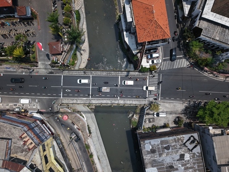 Aerial view of a busy road intersection and bridge over a canal with cars and motorcycles driving in Kecamatan Denpasar Barat Bali Indonesia. Aerial view of a busy road intersection and bridge over a canal with cars and motorcycles driving in Kecamatan Denpasar Barat Bali Indonesia.