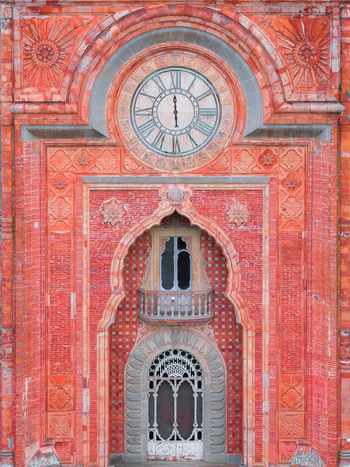 Aerial view of the ornate reddish pink facade of the Castello di Sammezzano featuring a large clock and intricate Moorish architectural details in Leccio Toscana Italy. Aerial view of the ornate reddish pink facade of the Castello di Sammezzano featuring a large clock and intricate Moorish architectural details in Leccio Toscana Italy.