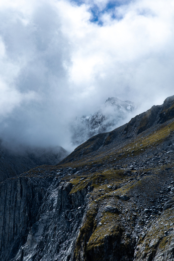 View of rugged cliffs meet the sky partially shrouded in ethereal mists creating a dramatic contrast of light and shadow Franz Josef Glacier West Coast Region New Zealand. View of rugged cliffs meet the sky partially shrouded in ethereal mists creating a dramatic contrast of light and shadow Franz Josef Glacier West Coast Region New Zealand.