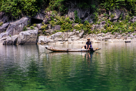 Meghalaya India 31 March 2023 View of a fisherman in a traditional wooden boat on the clear green waters of a river surrounded by rocky cliffs and lush vegetation. Meghalaya India 31 March 2023 View of a fisherman in a traditional wooden boat on the clear green waters of a river surrounded by rocky cliffs and lush vegetation.