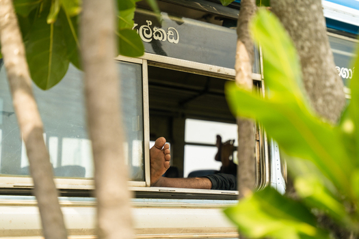 View of a passenger s bare feet resting on the window frame of a local bus framed by lush green tropical leaves in Galle Southern Province Sri Lanka. View of a passenger s bare feet resting on the window frame of a local bus framed by lush green tropical leaves in Galle Southern Province Sri Lanka.