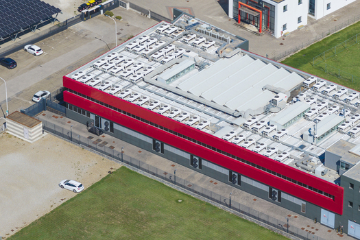 Aerial view of a modern data center building featuring numerous rooftop HVAC units and distinctive red architectural trim situated in a commercial area in Arezzo Tuscany Italy. Aerial view of a modern data center building featuring numerous rooftop HVAC units and distinctive red architectural trim situated in a commercial area in Arezzo Tuscany Italy.