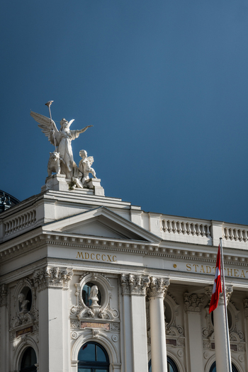 Zurich Switzerland 02 April 2023 View of the Schauspielhaus its elegant facade adorned with sculptures under a deep blue sky a Swiss flag gently waving. Zurich Switzerland 02 April 2023 View of the Schauspielhaus its elegant facade adorned with sculptures under a deep blue sky a Swiss flag gently waving.