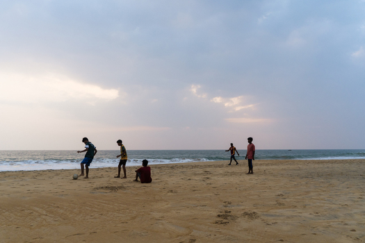 Sri Lanka 29 January 2026 View of local boys playing football on a sandy beach under an overcast sky at dusk.