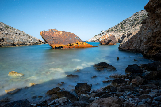 View of a rusted shipwreck resting in the clear turquoise waters of a secluded rocky cove in Lefkada Greece.